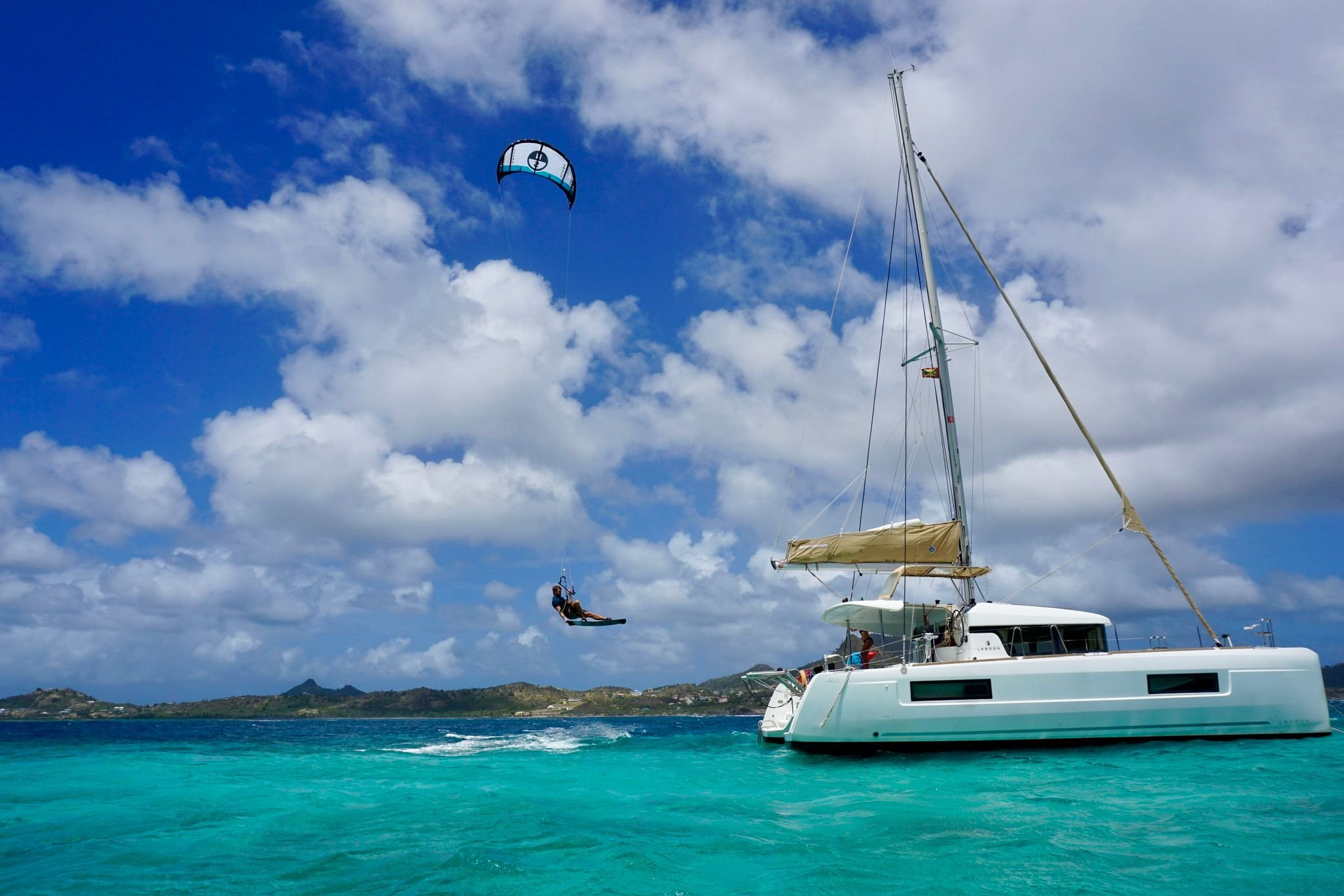 Kitesurfer jumping near catamaran in turquoise water