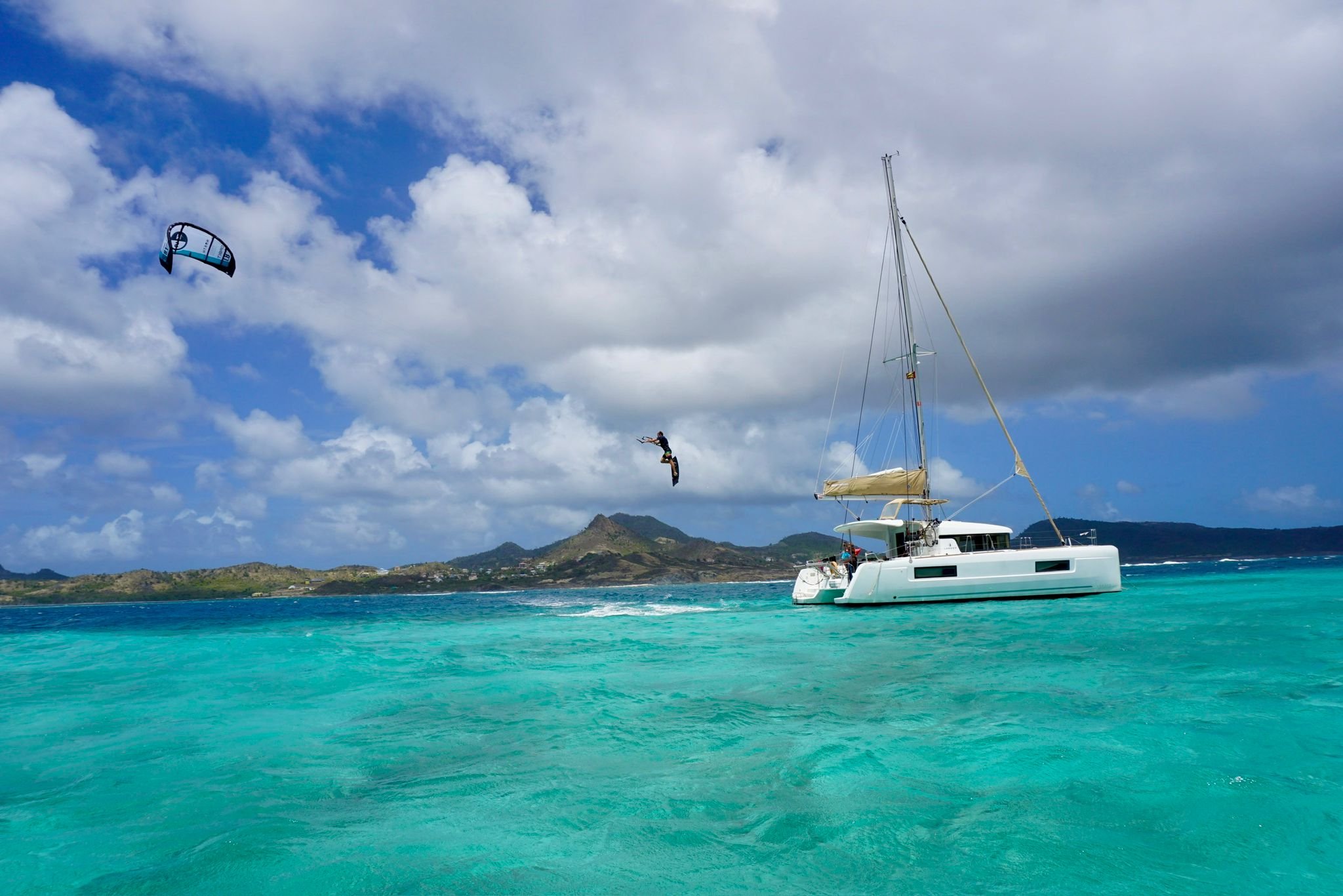 Kitesurfer jumping next to a catamaran in turquoise water