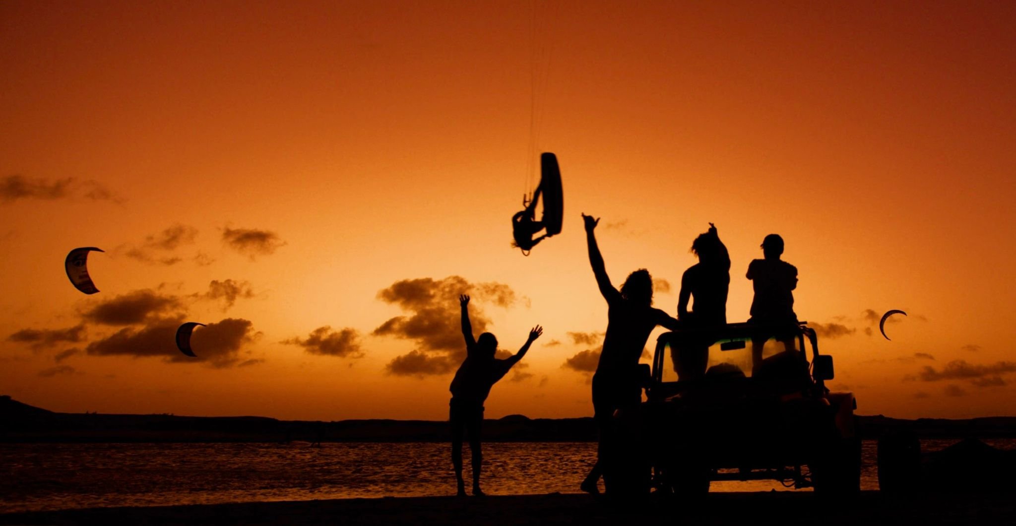 Friends watching kitesurfers at sunset from a beach buggy